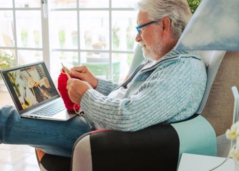 An old man sitting in a chair using a laptop.