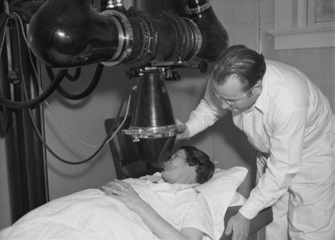 A woman looking at a man in a hospital bed.