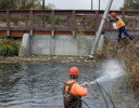 A man on a ladder in a river with a man on a bicycle.