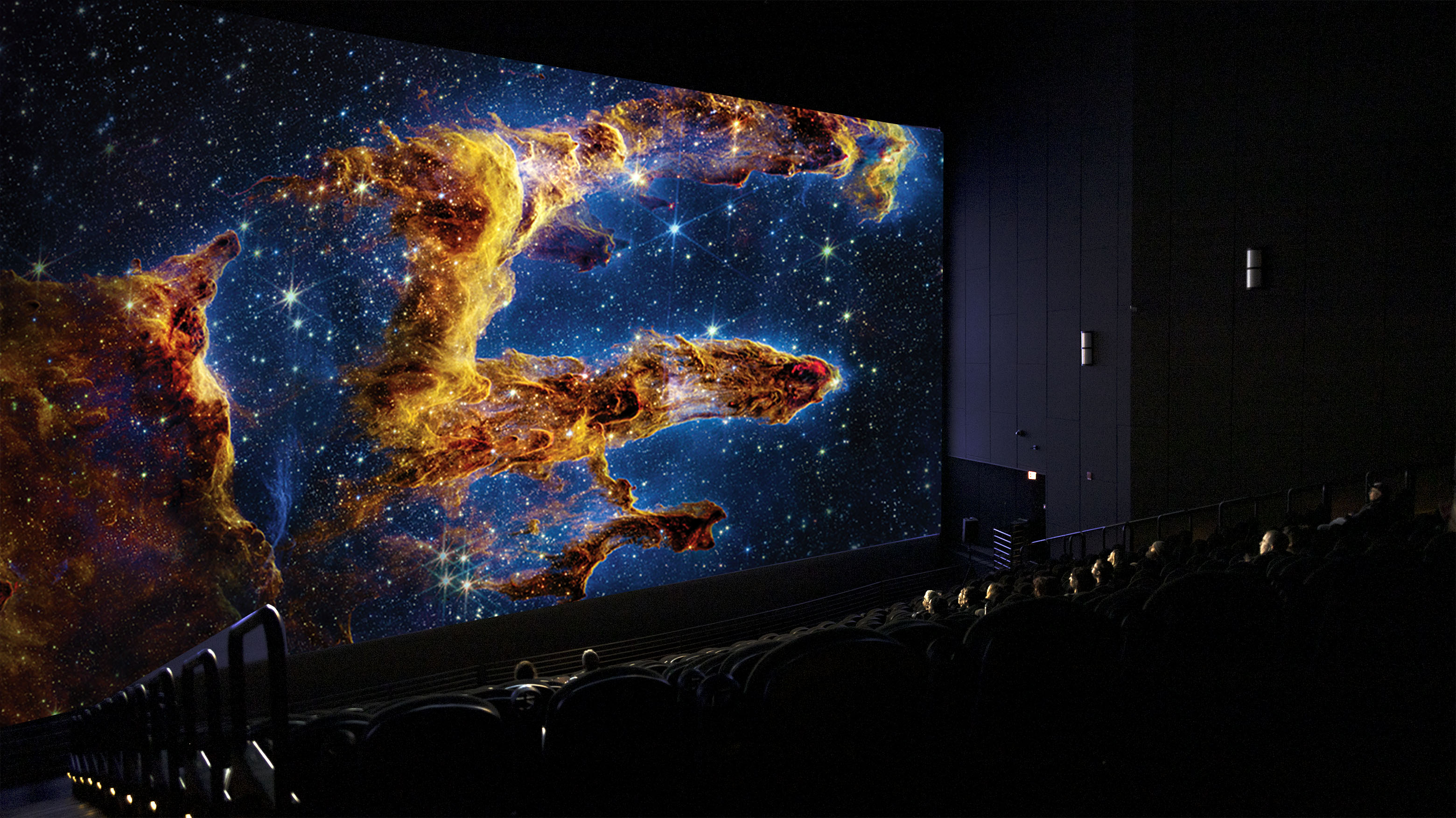 Partially full IMAX theatre with nebulae and space objects displaying on the IMAX screen