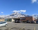 A parking lot with cars and a building with snow covered mountains in the background.