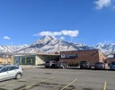 A parking lot with cars and a building with snow covered mountains in the background.
