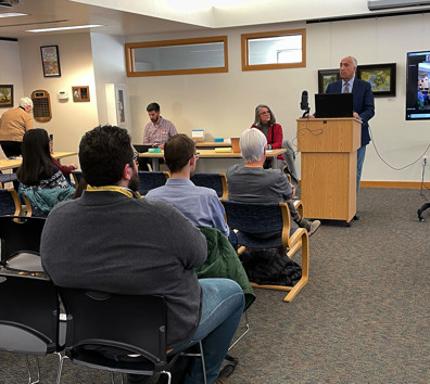 A group of people sitting in a room with a person standing in front of a screen.