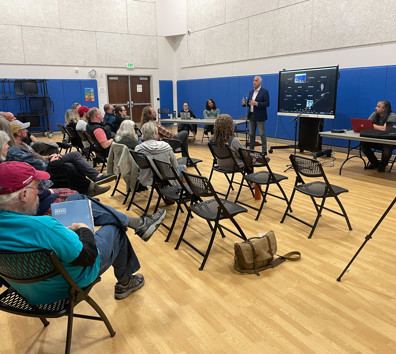 A group of people sitting in a room with a person standing in front of a screen.