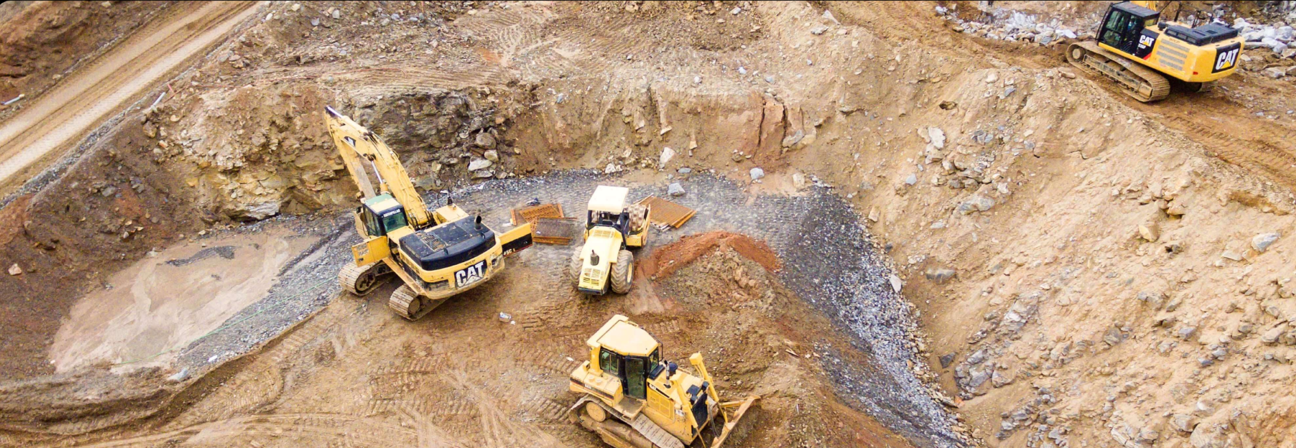 Several yellow construction vehicles in a dirt field.