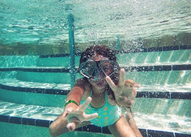 Young girl showing a peace sign while swimming under water.