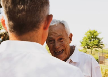 An older man smiling and speaking to a younger man.