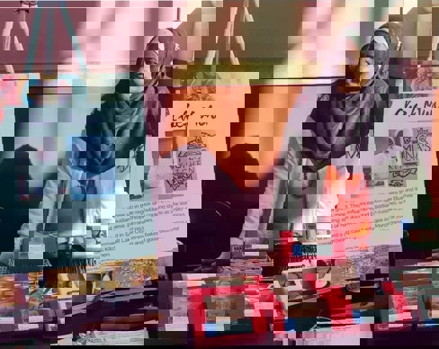 A person standing next to a table with books and a sign.