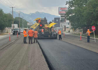 A group of men in orange vests standing on the side of a road.