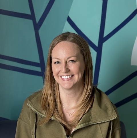 A person smiling in front of a blue wall.