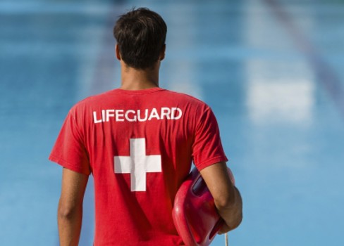 Lifeguard in a red shirt in front of a pool.