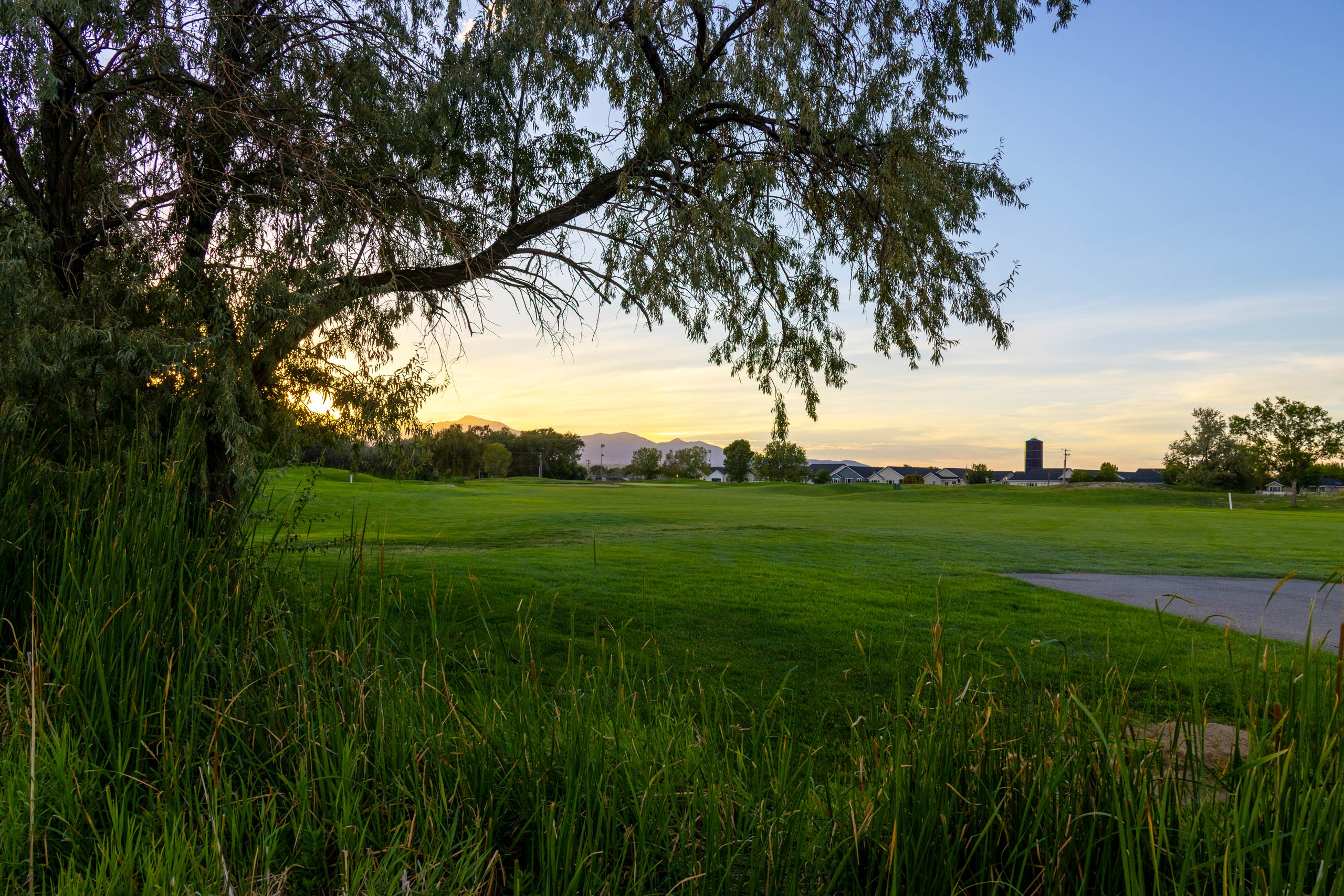 A fairway on Riverbend Golf Course in Riverton, Utah, with trees and buildings in the background.
