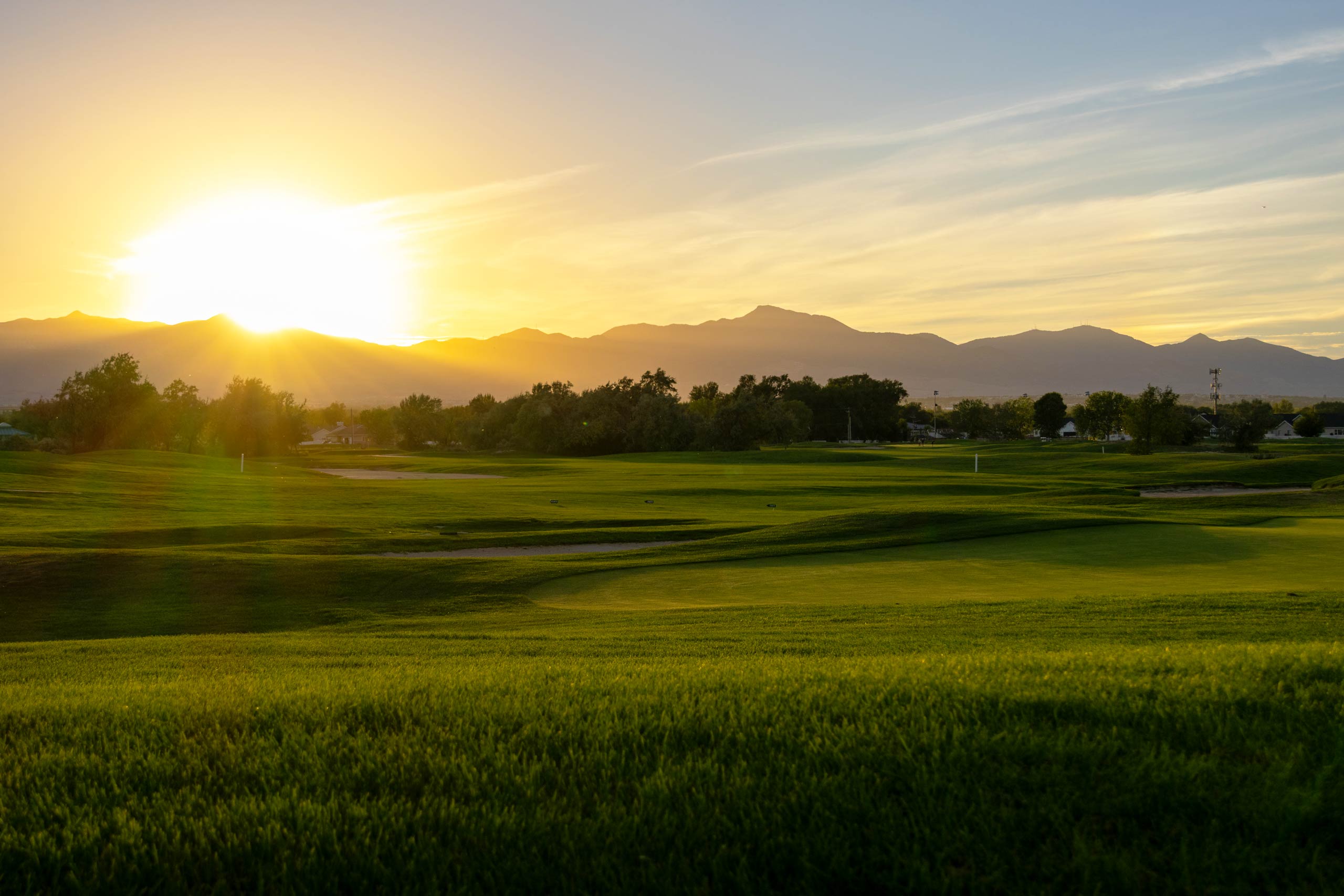 A large green fairway with trees and a sunset at Riverbend Golf Course in Salt Lake City.