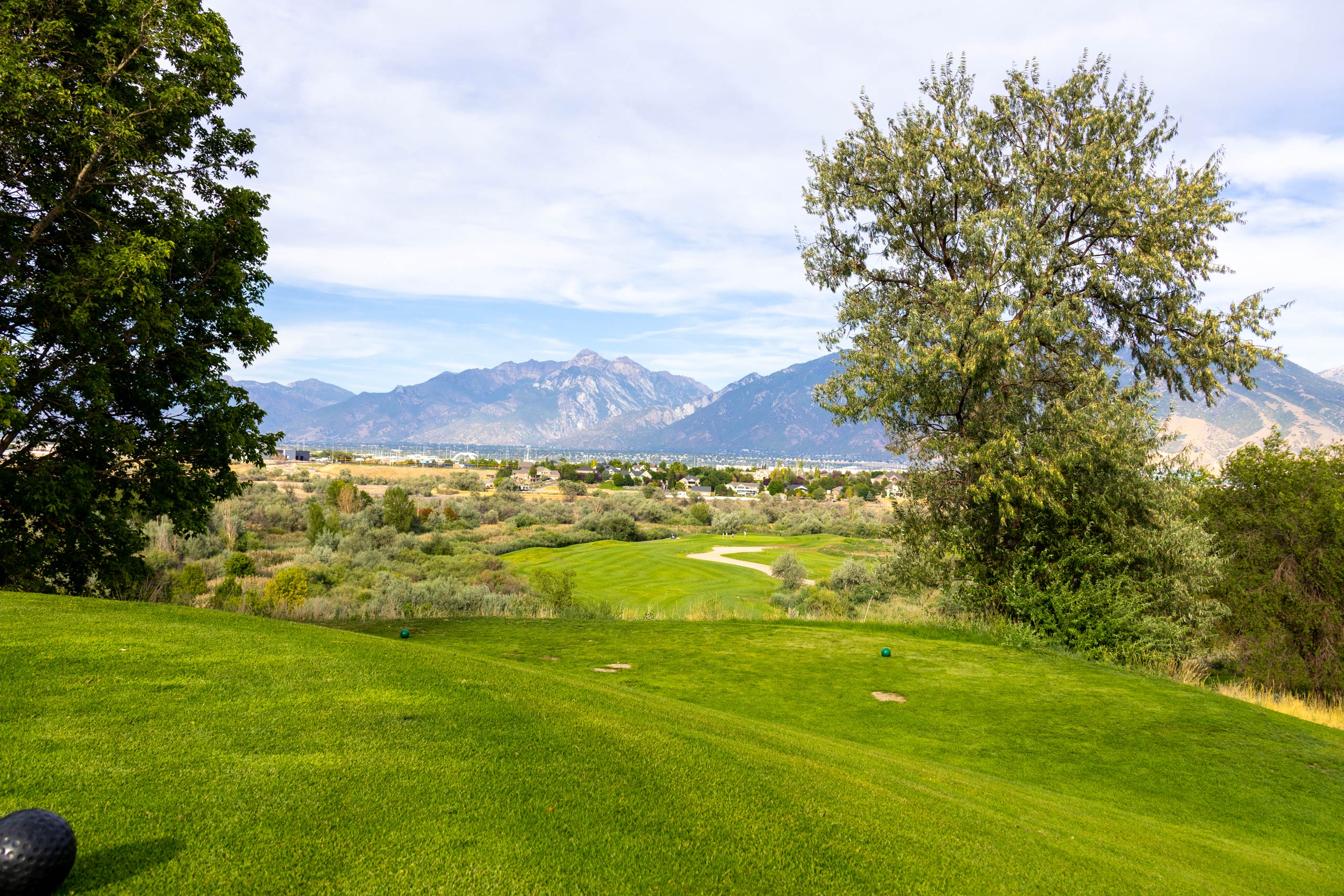 A fairway and green at Riverbend Golf Course in Riverton with mature trees and the Wasatch Mountains in the background.