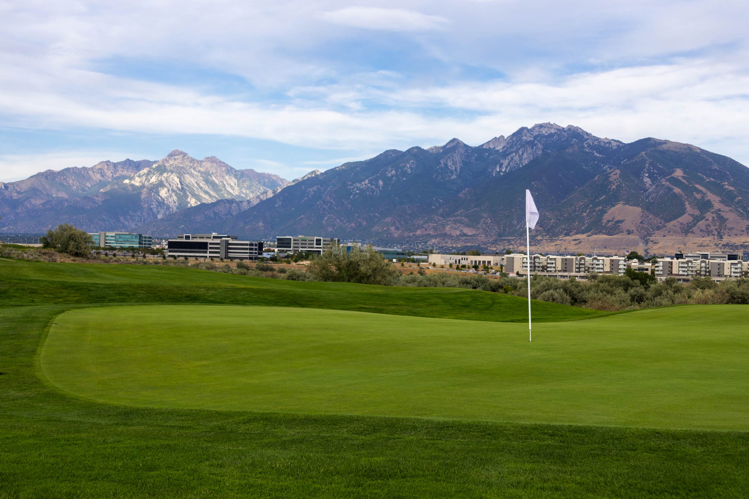A flag and green on Riverbend Golf Course in Riverton, Utah, with the city and mountains in the background.
