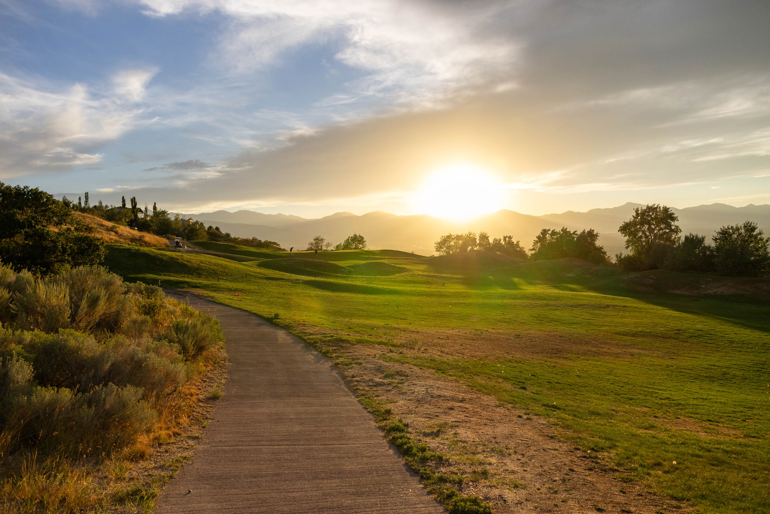 South Mountain golf course fairway at sunset with a golf cart path and trees on either side.