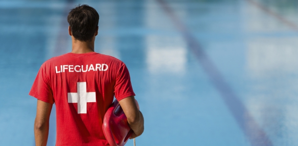 Lifeguard in a red shirt in front of a pool.